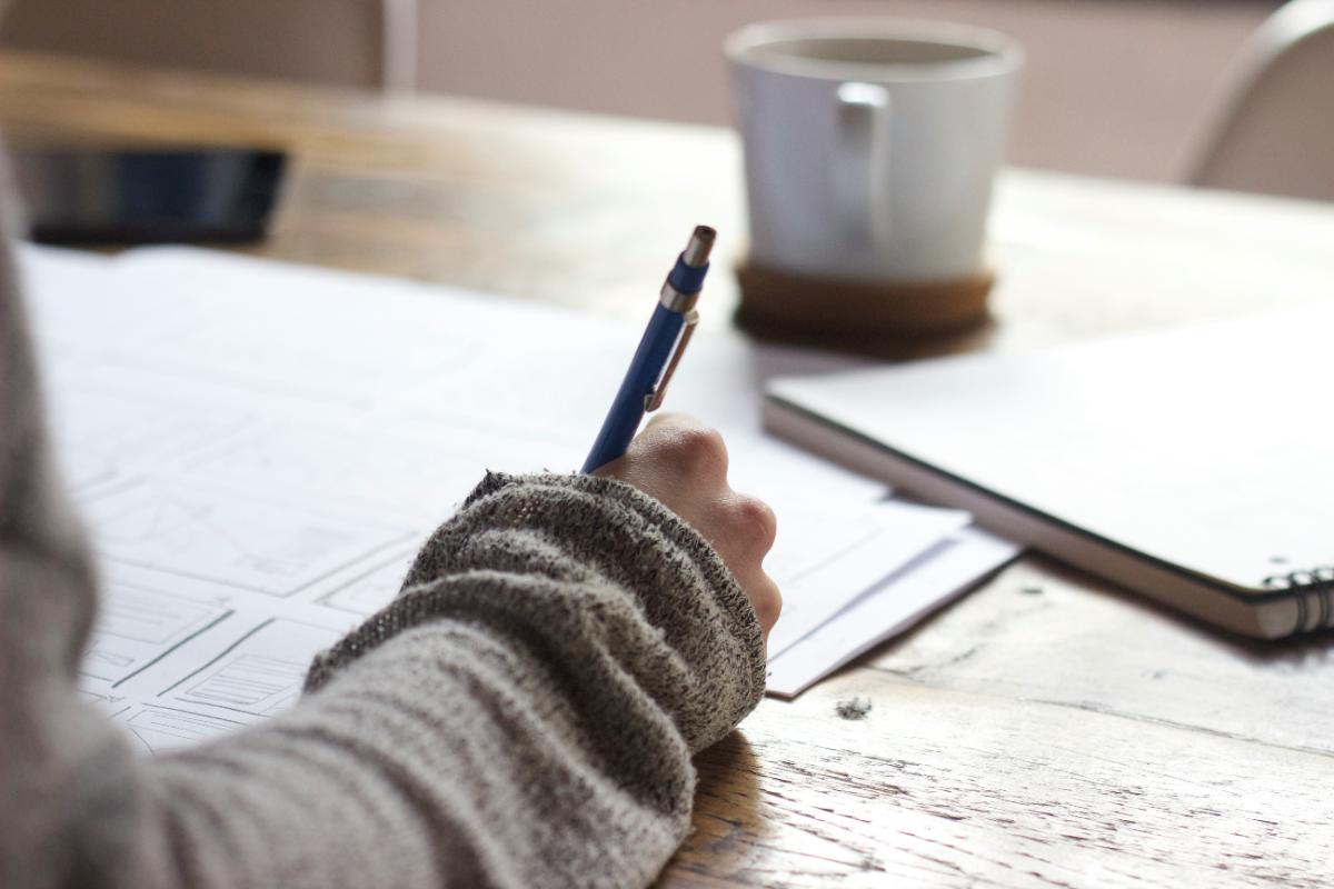 Persona escribiendo con calma en un cuaderno junto a una taza